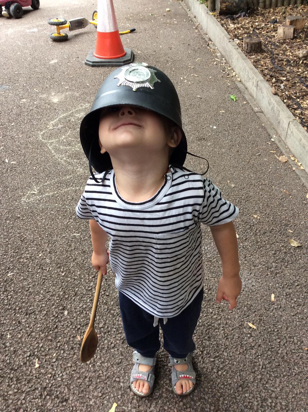 Child wearing oversized policeman's hat and holding a wooden spoon